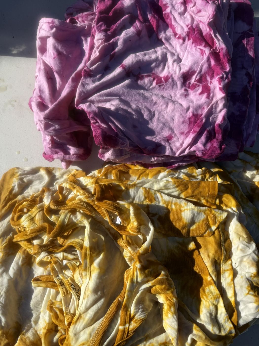 Stacks of pink and gold plant-dyed garments in daylight
